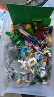 Top view of plastic bin filled with assorted loose LEGO bricks and baseplates in various colors and shapes.