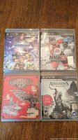 Four used PS3 games in cases laid side by side showing front cover art: NHL 13 with a hockey player, Kingdom Hearts 2.5 HD Remix with characters, Bioshock Infinite with red artistic cover, Assassin's Creed 3 with main character holding weapons.