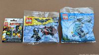 Three sealed Lego sets side by side including Lego Ninjago Movie minifigure pack, Lego Batman 30523 set with Batman and red dragon figure, and Lego City 30351 helicopter polybag set
