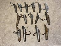 Overview of 15 metal maple syrup tree taps laid out on cement floor, all showing signs of rust and use.