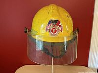 Front view of yellow firefighter helmet with clear visor and badge sticker showing FDNY 9-11 2001 with US and Canadian flags.