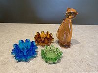 Set of one amber glass cat figurine and three swung glass bowls in blue, brown, and green.