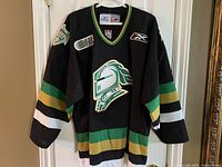 Front view of black London Knights jersey on hanger against white door