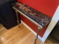 Full side view of narrow marble top hallway table against red wall showing polished veined marble top and gold tapered legs.
