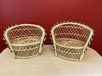 Pair of vintage wicker planter chairs with lattice backs and woven seats on wooden surface against red wall.