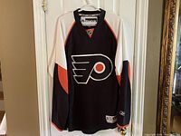 Front view of the Philadelphia Flyers hockey jersey hanging on a hanger showing the color scheme and logo.