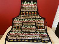 Photo of the full apron spread out on a flat surface showing detailed traditional Madeira patterns and pocket.