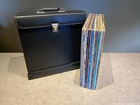 Black vinyl record carrying case alongside a stack of vinyl records.