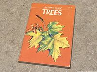 Front cover of vintage softcover book titled 'Trees' featuring illustration of maple leaves and seeds on orange background.