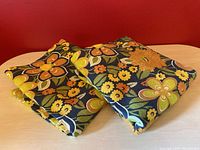 Two folded vintage floral print drapery panels with large flowers in orange, yellow, brown, and green shades.