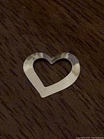 Close-up of hollow heart pendant shape on wood surface showing reflective hammered texture.
