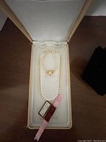Pearl necklace inside original cream jewelry case with tags and pink ribbon.