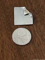 Front of vintage Birks square pin with folded corner detail next to a Canadian quarter for size reference.