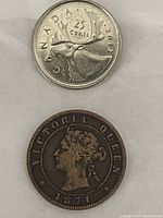 Front side of a 25 cents Canada coin compared for size next to the antique 1871 Prince Edward Island one cent coin with Queen Victoria portrait.