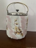Front angle of antique biscuit barrel showing hand-painted floral design, mottled pink and white glass, silver lid and handle.