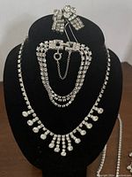 Photo showing the triple strand rhinestone bracelet with safety chain along with two necklaces and pairs of earrings on black display