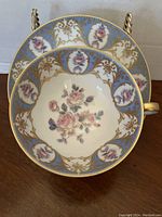 Top view of the porcelain teacup showing detailed rose floral hand painted inside with blue and gold accents on rim and handle