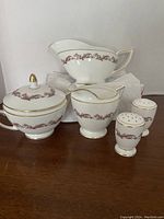 Full set of five porcelain serving pieces: gravy boat, covered sugar bowl, creamer, salt and pepper shakers all with gold trim and red-pink decorative motif arranged on dark wooden surface