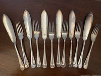 Complete set of 6 silver plated dessert/fish knives and 6 matching forks laid out on a wooden surface.