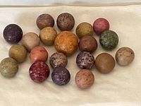 Top down view of 20 antique clay marbles arranged in 3 rows showing color variation and size differences.
