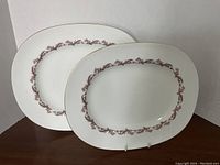 Two white oval porcelain serving platters with purple and gold patterned borders displayed upright.