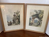 Photo showing both framed watercolor paintings side by side on a wooden surface, depicting Italian lakeside scenes with detailed greenery and architecture.