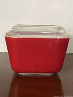 Front view of the cherry red Pyrex jar with clear ribbed glass lid on a dark wooden surface.