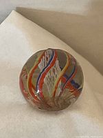 Front view of early clear glass marble showing white latticino swirl with colored stripes inside.