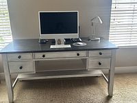 Photo of wooden desk with dark top surface, five drawers with black knobs, holding an iMac, keyboard, mouse, speakers, and a desk lamp.