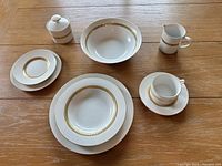 Overall view of set showing dinner plate, soup bowl, cup with saucer, sugar bowl with lid, and creamer, all with 22ct gold band detail on white ceramic.