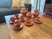 Photo showing a terracotta coffee/tea set on a wooden table including teapot, creamers, sugar bowls, cups and saucers.
