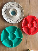 Top-down view of three party trays: one white ceramic 'Paradise Diner' chip and dip platter and two plastic compartmentalized trays in red and green.