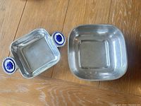 Two metal trays on wooden table, one with decorative blue and white ceramic handles and the other plain square metal tray.