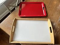 Two rectangular trays on wooden table, one red and one wood frame with white surface