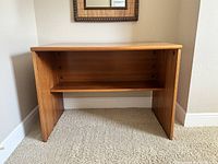 Small wooden desk placed against a corner wall, showing the front view with its shelf and solid panel legs visible.