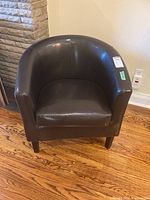 Front view of dark brown faux leather bucket chair showing curved back and seat cushion.