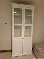 Front view of the white wooden cabinet showing two glass-paneled doors and lower solid panel doors with metal knob handles.