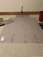 Top view of clear plastic chair mat on beige carpet showing textured surface and lip cutout.