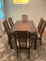 Six wood framed dining chairs arranged around a matching dining table displaying dark wood finish with wicker backs and fabric seats.