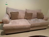 Front view of a beige ultra suede fabric couch with cushions. Three back cushions and three smaller brown throw pillows are arranged on it. Small spots visible on fabric surface.