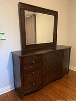 Front angle view of the dark wooden dresser with attached mirror showing drawer layout and carved frame design.