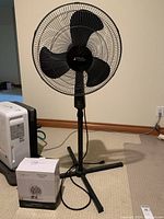 Front view of Atlantic Breeze stand up fan 45 with Mainstay electric fan heater box in foreground on carpeted floor.