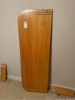 Full view of the wood headboard standing vertically, showing rounded corner and metal inlays.