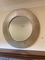 Front view of the round decorative mirror showing textured ribbed metallic frame and clear center reflective surface hanging above a fireplace mantel.