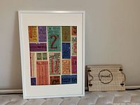 Framed print and wood sign displayed on floor against wall, showing colorful ticket collage and wood burned sign design