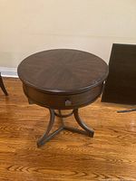 Overall angled view of dark stain round side table with curved leg supports and drawer visible