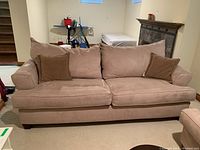 Front view of tan ultra suede sofa bed with two cushions and two accent pillows in a basement room
