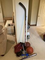 Photo of Sher-Wood Pro hockey stick standing vertically next to two basketballs, hand weights, and a baseball bat on carpet.