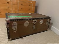 Full front and top angled view of the rectangular vintage trunk showing metal latches and surface wear.