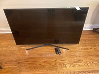 Front view of TV on stand with both remotes on hardwood floor